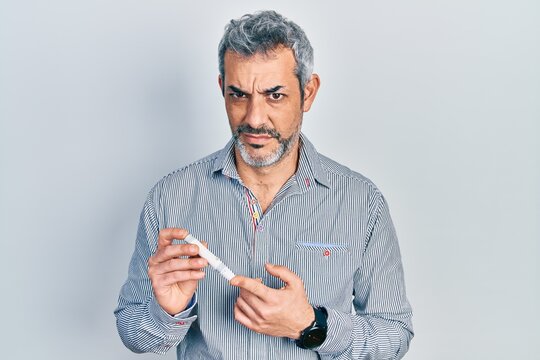 Handsome middle age man with grey hair holding glucometer device clueless and confused expression. doubt concept.