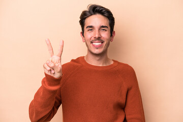 Young caucasian man isolated on beige background showing victory sign and smiling broadly.