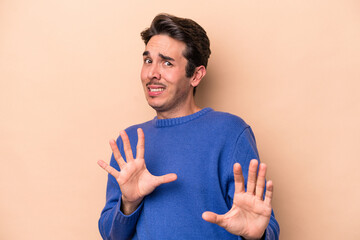 Young caucasian man isolated on beige background rejecting someone showing a gesture of disgust.