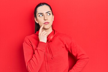 Beautiful woman with blue eyes wearing gym clothes and headphones serious face thinking about...