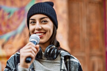 Young hispanic woman smiling happy using headphones and microphone at the city.