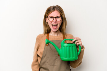 Young gardener woman holding a sprinkler isolated on white background screaming very angry and aggressive.