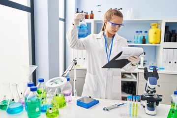 Fototapeta premium Young blonde woman wearing scientist uniform holding test tube and clipboard at laboratory