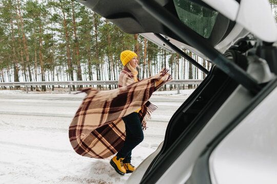 Woman with blanket standing by car in winter