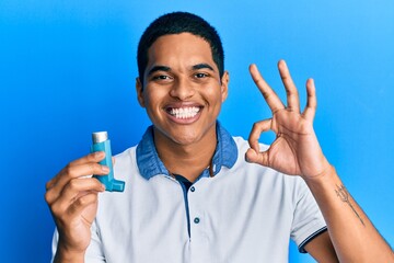 Young handsome hispanic man holding medical asthma inhaler doing ok sign with fingers, smiling...