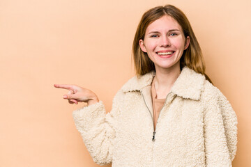 Young English woman isolated on beige background smiling cheerfully pointing with forefinger away.