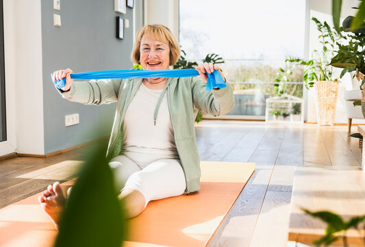 Cheerful senior woman with resistance band working out at home