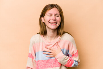 Young English woman isolated on beige background laughs out loudly keeping hand on chest.