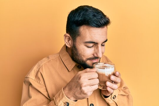 Handsome hispanic man enjoying a cup of coffee over yellow background