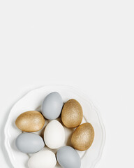 Painted Easter eggs golden, gray, beige colored on white plate, light background with copy space. Chicken egg pastel shades. Easter holiday food concept, minimal design aesthetic flat lay
