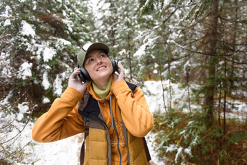 Smiling woman looking up listening music on headphones in winter forest