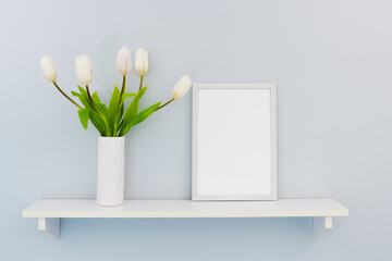 A white vertical frame stands on a shelf with white tulips