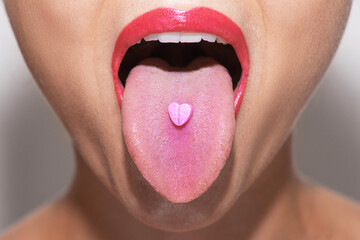 Half of female face with heart shaped pill on tongue - obrazy, fototapety, plakaty