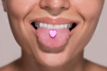 Half of female face with heart shaped pill on tongue