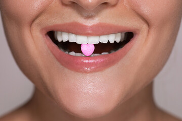 Half of female face with heart shaped pill on tongue