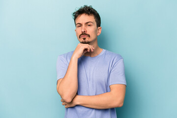 Young caucasian man isolated on blue background suspicious, uncertain, examining you.