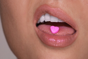Half of female face with heart shaped pill on tongue.
