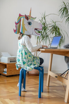 Girl in unicorn mask using laptop at home