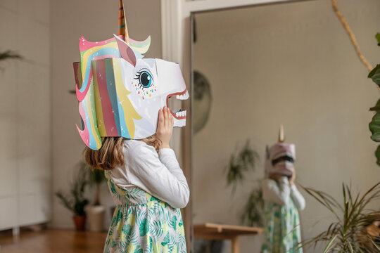 Girl with unicorn mask looking in mirror at home