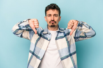 Young caucasian man isolated on blue background showing a dislike gesture, thumbs down....