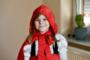 Little preschool girl dressed in red riding hood costume. Happy child, indoors, playing fairytales. - obrazy, fototapety, plakaty