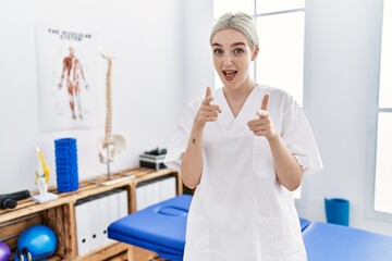 Young caucasian woman working at pain recovery clinic pointing fingers to camera with happy and funny face. good energy and vibes.