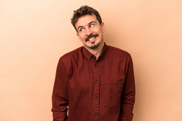 Young caucasian man isolated on beige background laughs and closes eyes, feels relaxed and happy.