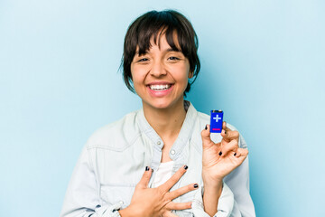 Young hispanic woman holding a batterie isolated on blue background laughing and having fun.