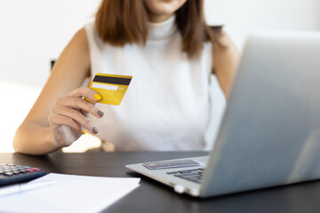 Woman holding credit card using laptop at home and shopping online. Financial planning ideas and expenses.