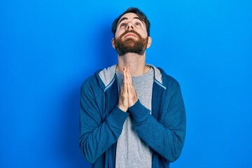 Caucasian man with beard wearing casual sweatshirt begging and praying with hands together with...