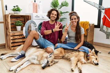 Young hispanic couple doing laundry with dogs showing and pointing up with fingers number seven while smiling confident and happy.