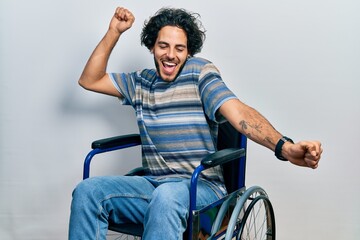 Handsome hispanic man sitting on wheelchair dancing happy and cheerful, smiling moving casual and...