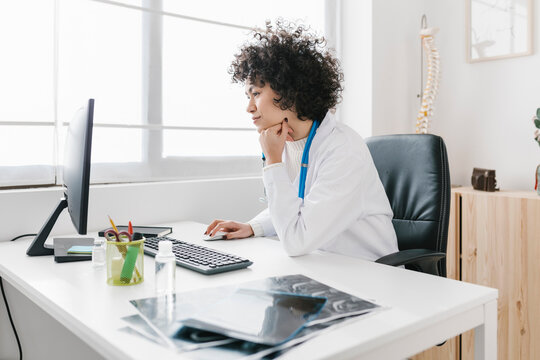 Doctor sitting with hand on chin using computer at medical clinic