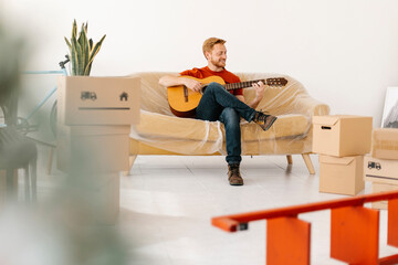 Young man practicing guitar sitting on sofa at home