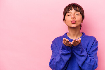 Young hispanic woman isolated on pink background folding lips and holding palms to send air kiss.