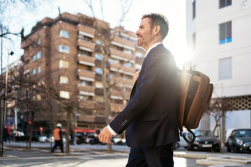 Smiling businessman with backpack in city