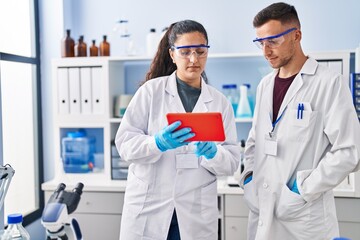 Man and woman wearing scientist uniform using touchpad at laboratory