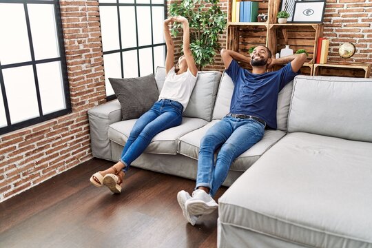 Man and woman couple relaxed with hands on head sitting on sofa at home