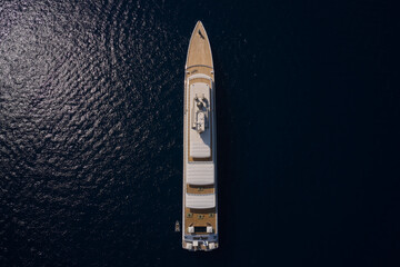 Big yacht for millionaires in the sea drone view. Luxurious white mega yacht on dark water in the reflection of the sun top view. Big white super ship in the dark ocean aerial view.
