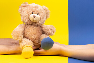 Hand holding teddy bear with different socks on yellow and blue background. World Down Syndrome Day...