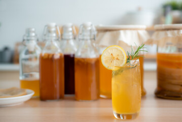 Kombu tea in a glass with ice, lemon slices and rosemary leaves, Homemade fermented raw kombucha tea in bottles and glass jars mix with fruit juice and scoby on table.Healthy natural probiotic drink.