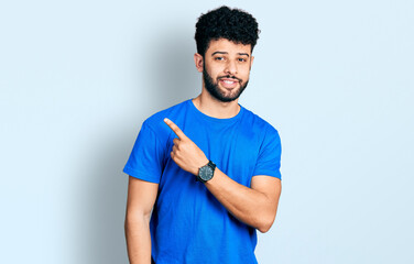 Young arab man with beard wearing casual blue t shirt pointing with hand finger to the side showing advertisement, serious and calm face