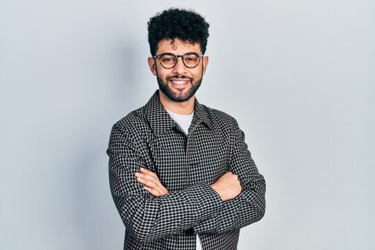 Young arab man with beard wearing glasses with arms crossed gesture smiling with a happy and cool smile on face. showing teeth.