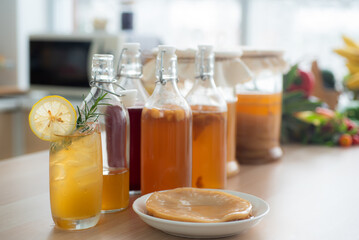 Kombu tea in a glass with ice, lemon slices and rosemary leaves, Homemade fermented raw kombucha tea in bottles and glass jars mix with fruit juice and scoby on table.Healthy natural probiotic drink.