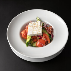 Fresh Greek salad - feta cheese, tomatoes, cucumber, red pepper, black olives and onion on a black background