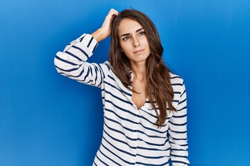 Fototapeta premium Young hispanic woman standing over blue isolated background confuse and wondering about question. uncertain with doubt, thinking with hand on head. pensive concept.