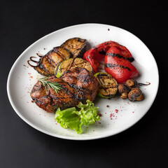 Pork steak with grilled vegetables on a black background