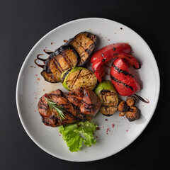 Pork steak with grilled vegetables on a black background.