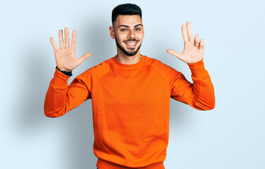 Fototapeta premium Young hispanic man with beard wearing casual orange sweater showing and pointing up with fingers number eight while smiling confident and happy.