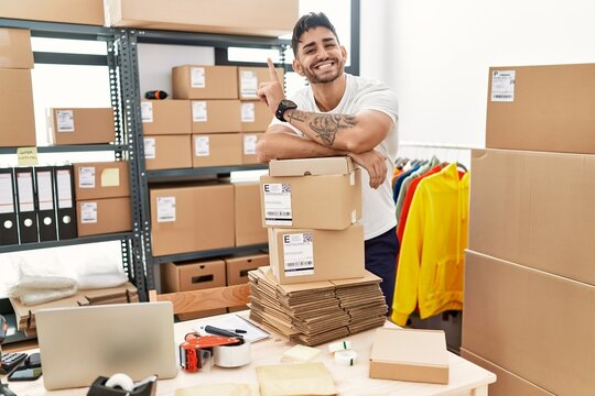Young hispanic man working at small business ecommerce surprised with an idea or question pointing finger with happy face, number one